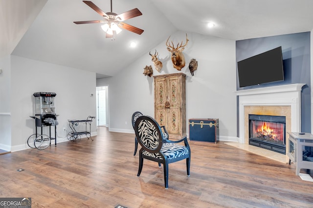 living area featuring ceiling fan, a tiled fireplace, wood finished floors, and baseboards