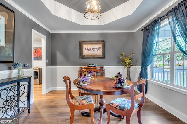 dining room featuring baseboards, a raised ceiling, ornamental molding, wood finished floors, and a notable chandelier