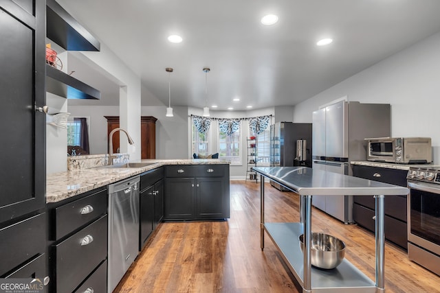 kitchen featuring light stone counters, decorative light fixtures, stainless steel appliances, dark cabinetry, and a sink