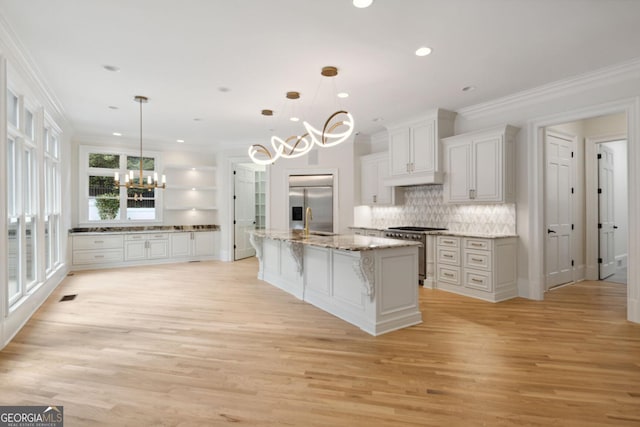 kitchen with decorative light fixtures, light hardwood / wood-style floors, stainless steel appliances, and a large island with sink