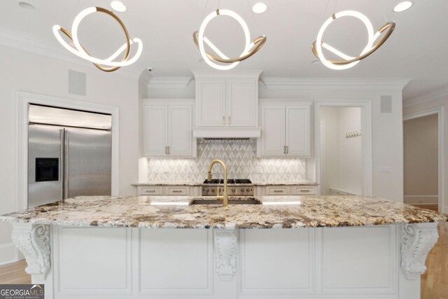 kitchen featuring a center island with sink, light stone countertops, white cabinetry, and built in refrigerator