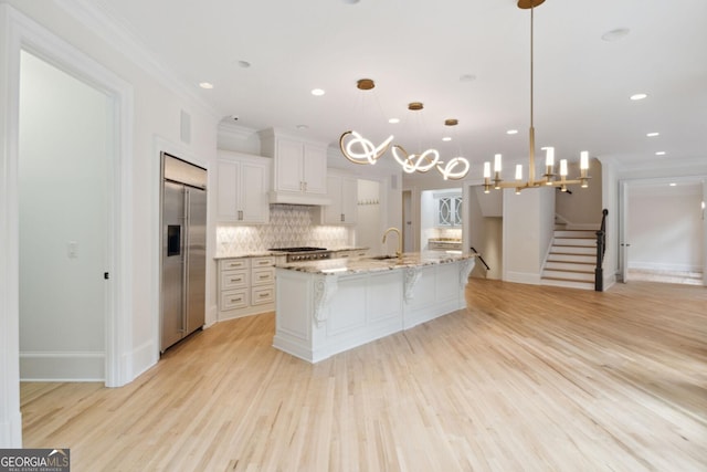 kitchen with pendant lighting, a large island with sink, light hardwood / wood-style flooring, white cabinetry, and built in fridge