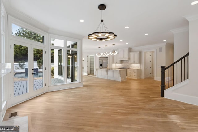 interior space with a chandelier, light wood-type flooring, crown molding, and french doors