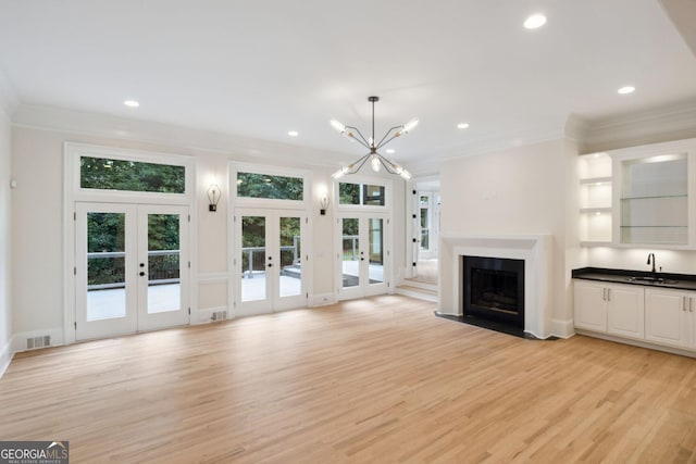 unfurnished living room with light hardwood / wood-style floors, an inviting chandelier, crown molding, and french doors