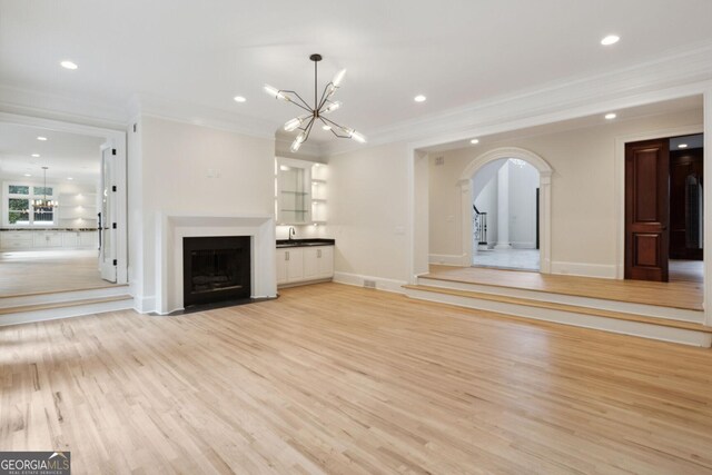 unfurnished living room with a chandelier, light hardwood / wood-style flooring, ornamental molding, and sink