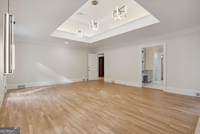 unfurnished room with a tray ceiling, crown molding, and light wood-type flooring