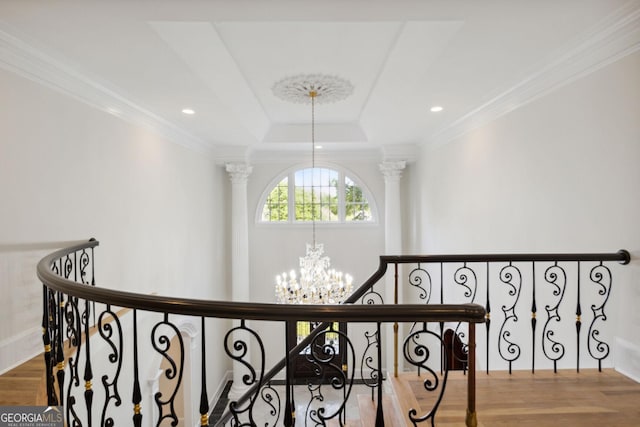 corridor featuring hardwood / wood-style floors, crown molding, ornate columns, a tray ceiling, and a chandelier