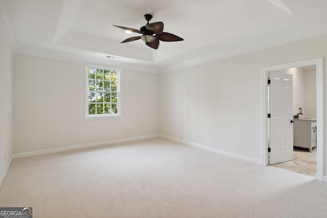 empty room with a raised ceiling, light carpet, crown molding, and ceiling fan