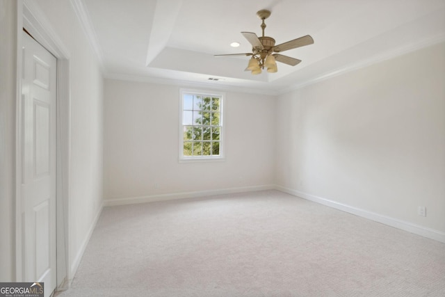 empty room featuring light carpet, a raised ceiling, ceiling fan, and crown molding