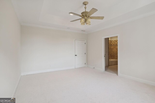 empty room featuring a tray ceiling, ceiling fan, light carpet, and ornamental molding