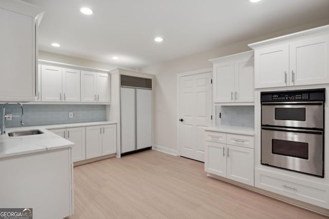 kitchen with double oven, tasteful backsplash, white cabinetry, and sink