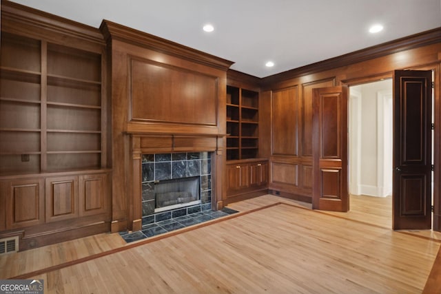 unfurnished living room with wood-type flooring, built in features, crown molding, and a tiled fireplace