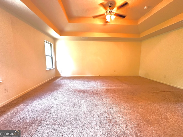 carpeted empty room with a raised ceiling and ceiling fan