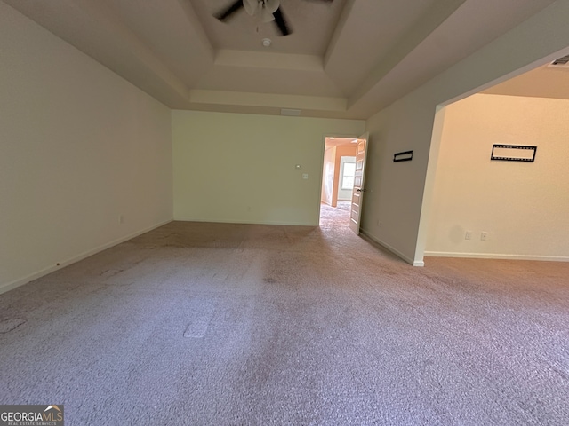 spare room featuring a raised ceiling, ceiling fan, and light carpet