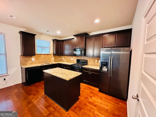 kitchen featuring black appliances, hardwood / wood-style flooring, a kitchen island, and dark brown cabinetry