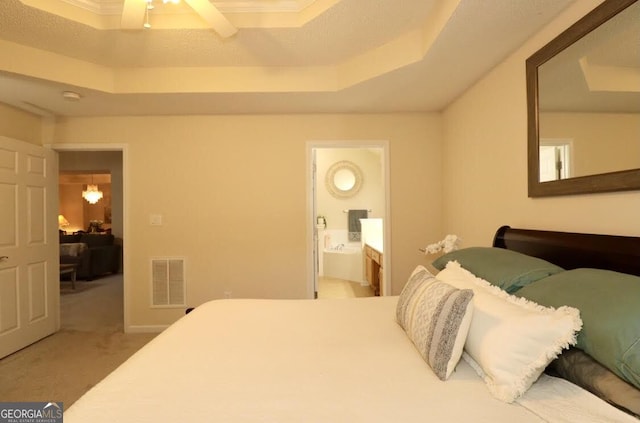 carpeted bedroom with a tray ceiling, visible vents, connected bathroom, and ceiling fan