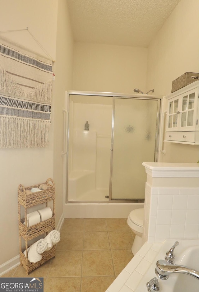 bathroom with toilet, a shower stall, a textured ceiling, baseboards, and tile patterned floors