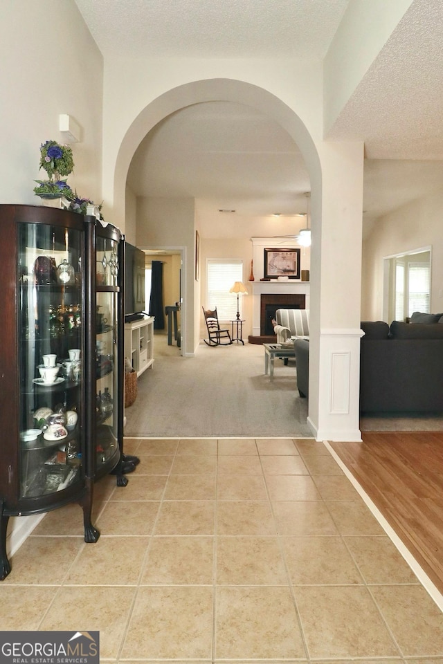 corridor featuring plenty of natural light, tile patterned flooring, arched walkways, and a textured ceiling