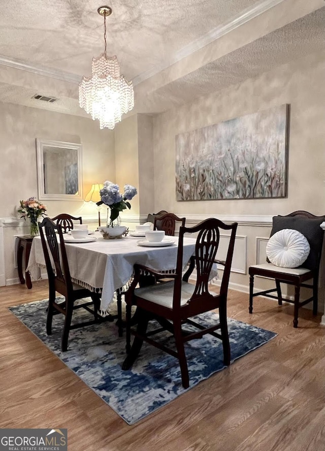 dining room with a chandelier, a textured ceiling, wood finished floors, and visible vents