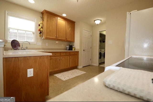 kitchen featuring brown cabinets, light countertops, a sink, and washing machine and clothes dryer