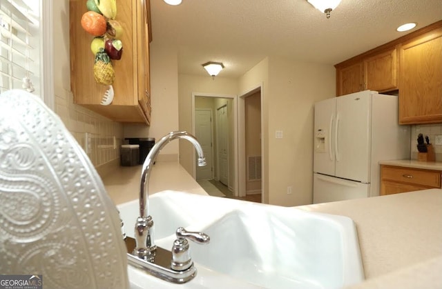 kitchen featuring white refrigerator with ice dispenser, decorative backsplash, brown cabinets, light countertops, and a textured ceiling