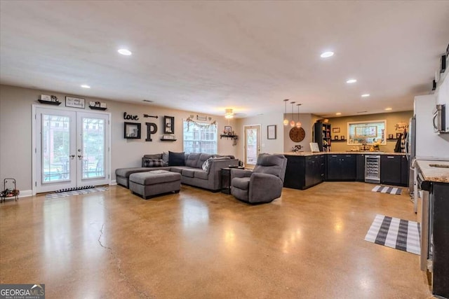 living room featuring plenty of natural light, concrete floors, beverage cooler, and french doors