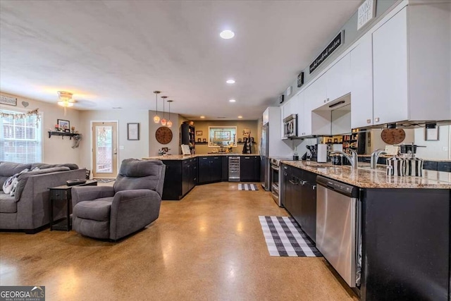 kitchen featuring pendant lighting, stainless steel appliances, kitchen peninsula, white cabinetry, and light stone counters