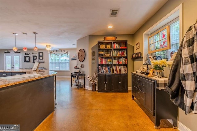 interior space with a healthy amount of sunlight, light stone counters, dark brown cabinetry, and hanging light fixtures