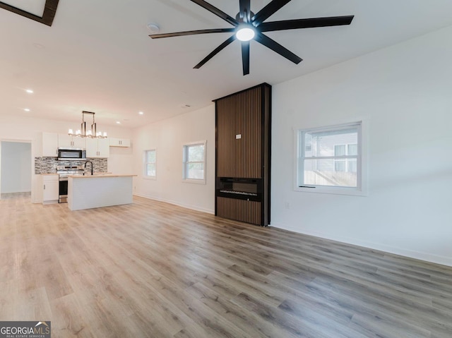 unfurnished living room featuring ceiling fan with notable chandelier, light wood-type flooring, and sink