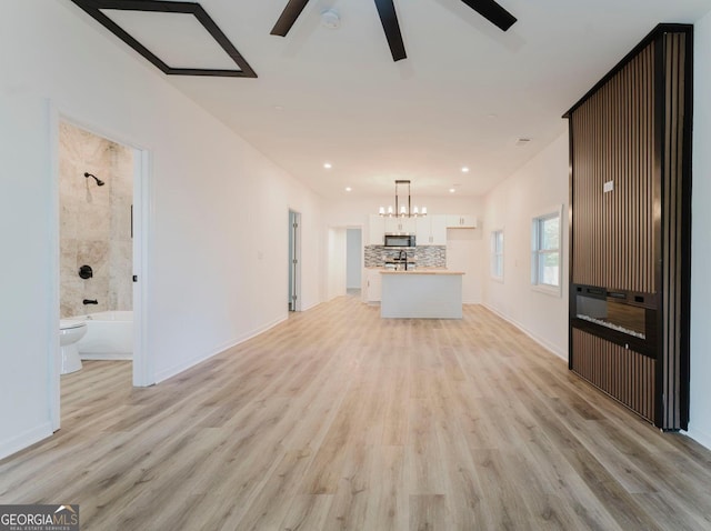 unfurnished living room with ceiling fan with notable chandelier and light hardwood / wood-style flooring