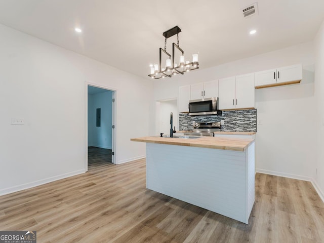 kitchen with butcher block countertops, a kitchen island with sink, white cabinets, and appliances with stainless steel finishes