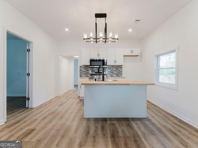 kitchen with sink, hanging light fixtures, light hardwood / wood-style flooring, an island with sink, and white cabinets