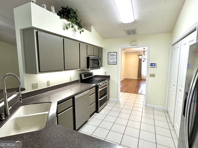 kitchen with gray cabinetry, light tile patterned floors, stainless steel appliances, sink, and a textured ceiling