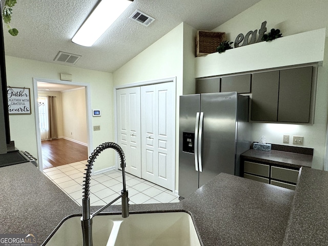 kitchen featuring light hardwood / wood-style flooring, sink, lofted ceiling, stainless steel fridge, and a textured ceiling