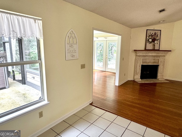 unfurnished living room with lofted ceiling, light hardwood / wood-style flooring, a high end fireplace, and a textured ceiling