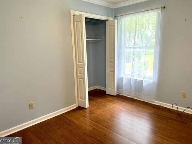 unfurnished bedroom with crown molding, dark wood-type flooring, and a closet