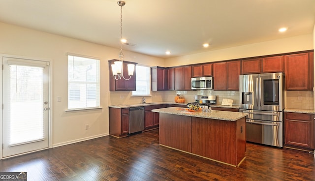 kitchen featuring light stone counters, stainless steel appliances, a center island, and hanging light fixtures