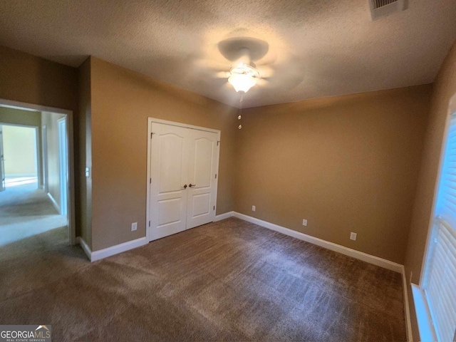 unfurnished bedroom with a closet, a textured ceiling, dark carpet, and ceiling fan