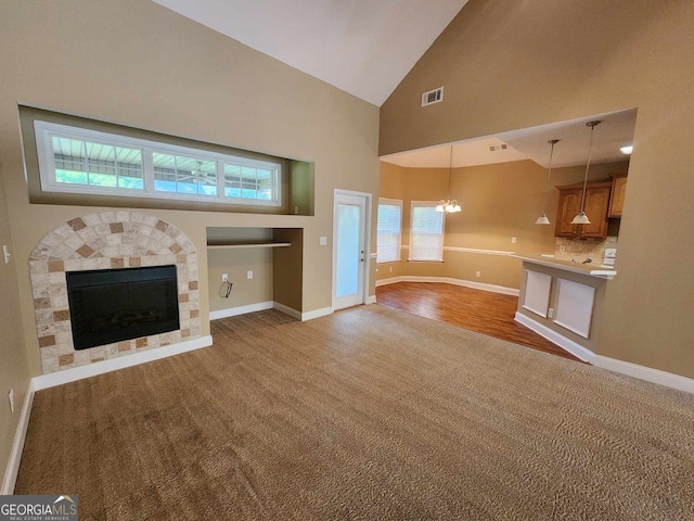 unfurnished living room with high vaulted ceiling, light colored carpet, and a notable chandelier