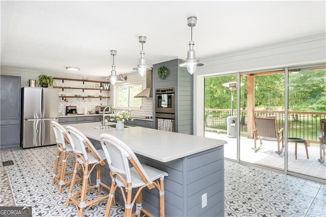 kitchen featuring gray cabinets, light countertops, open shelves, wall chimney exhaust hood, and stainless steel appliances