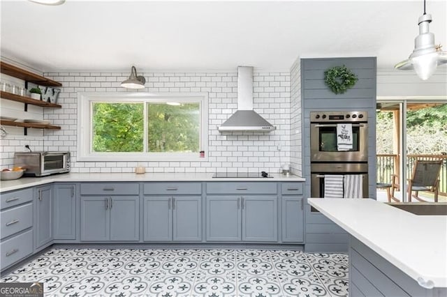 kitchen with light countertops, wall chimney exhaust hood, stainless steel double oven, black electric stovetop, and a toaster