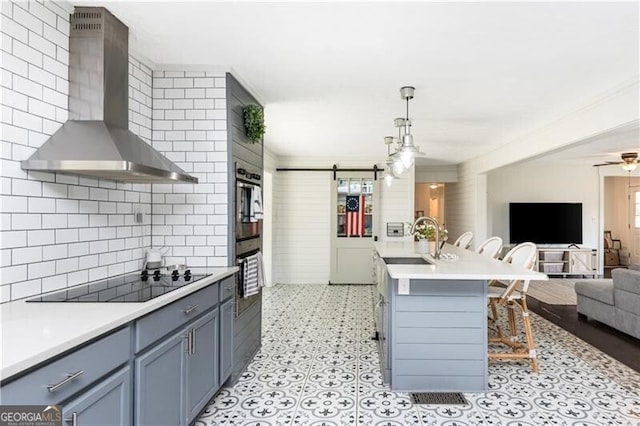 kitchen with black electric stovetop, sink, a breakfast bar, wall chimney exhaust hood, and a barn door