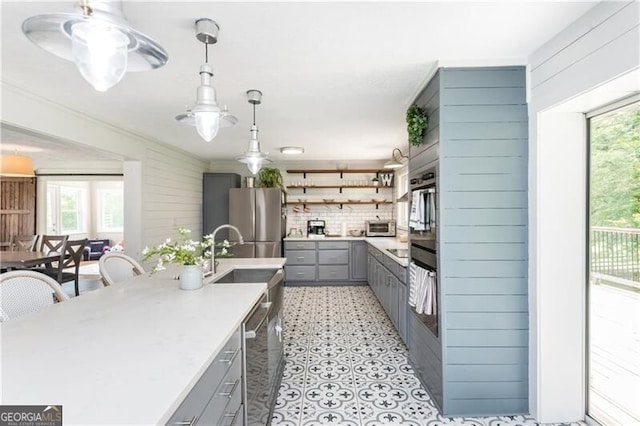 kitchen with gray cabinetry, light countertops, open shelves, and stainless steel appliances