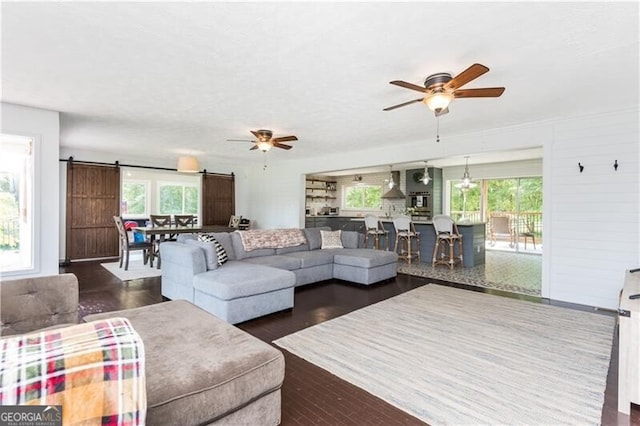 living room featuring a barn door, ceiling fan, wood walls, and dark wood-type flooring