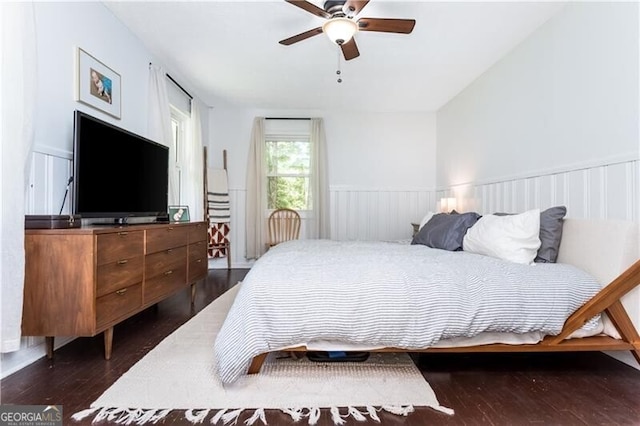 bedroom with a wainscoted wall, dark wood-type flooring, and a ceiling fan