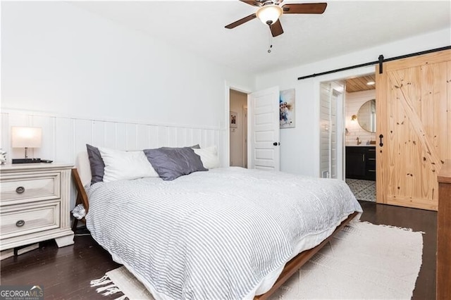 bedroom with dark wood-type flooring, ceiling fan, a barn door, and ensuite bathroom