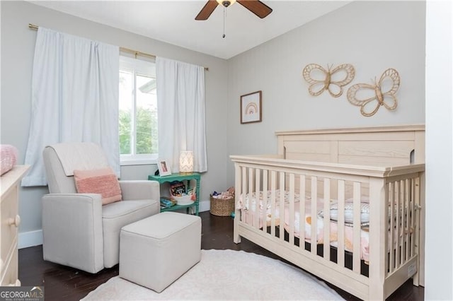 bedroom with wood finished floors, a crib, and a ceiling fan