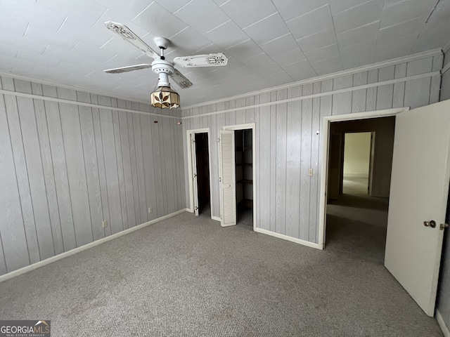 unfurnished bedroom with carpet, ceiling fan, wood walls, and a closet