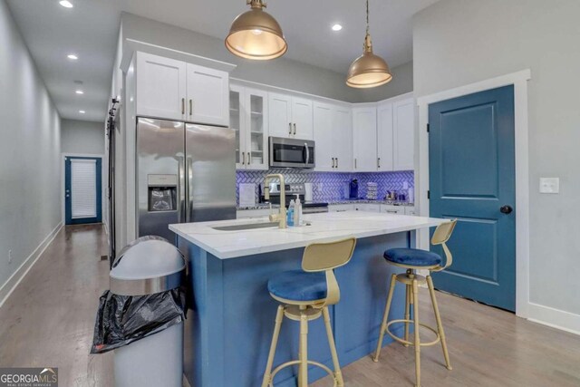 kitchen with decorative light fixtures, stainless steel appliances, a center island with sink, and white cabinetry