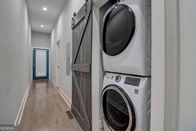 washroom featuring a barn door, light wood-type flooring, and stacked washer / drying machine